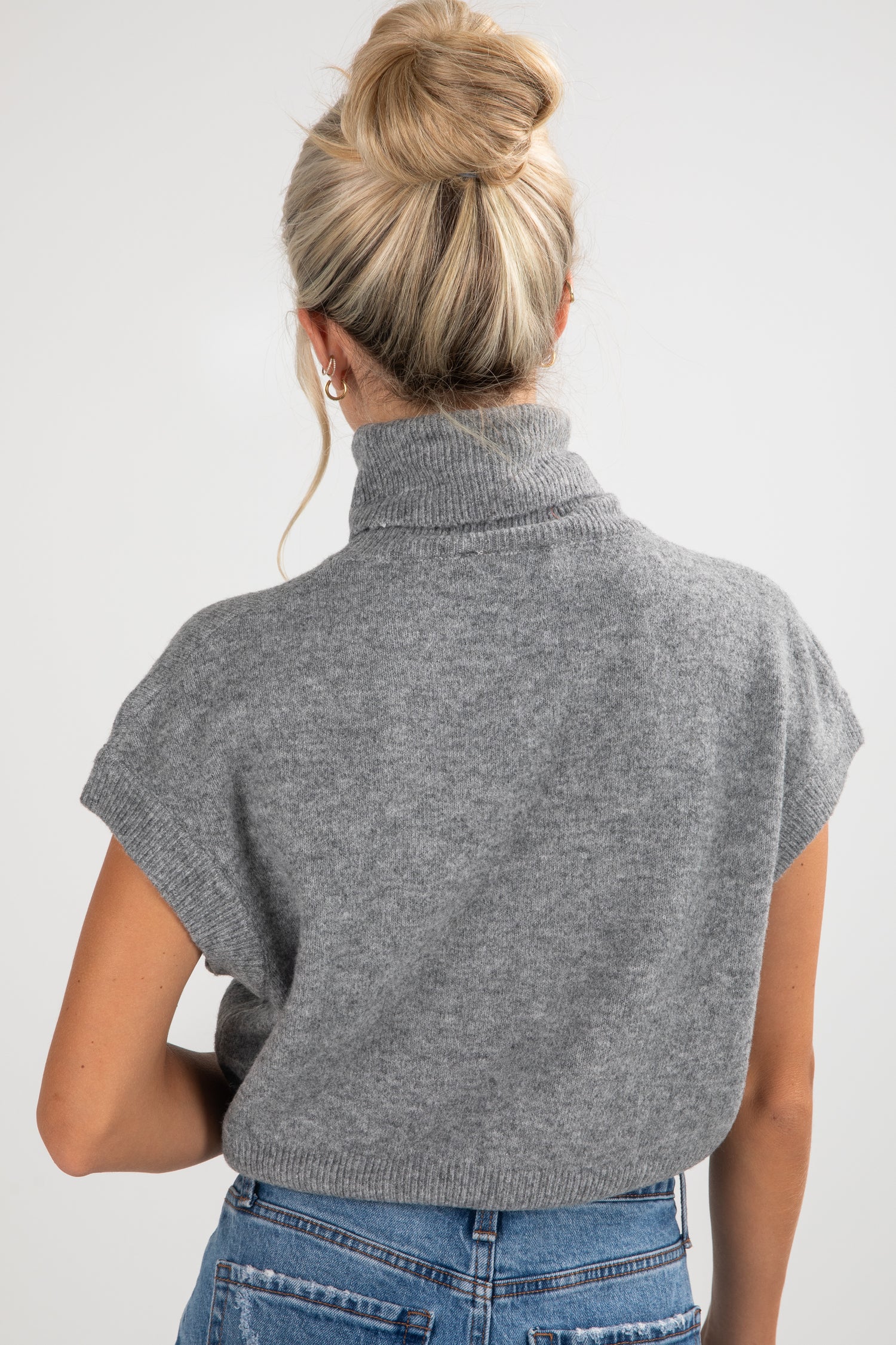 Person wearing a gray turtleneck sweater over a blue top on a white background