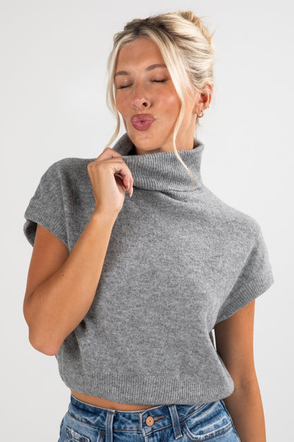 Woman wearing a gray cowl-neck sweater against a white background