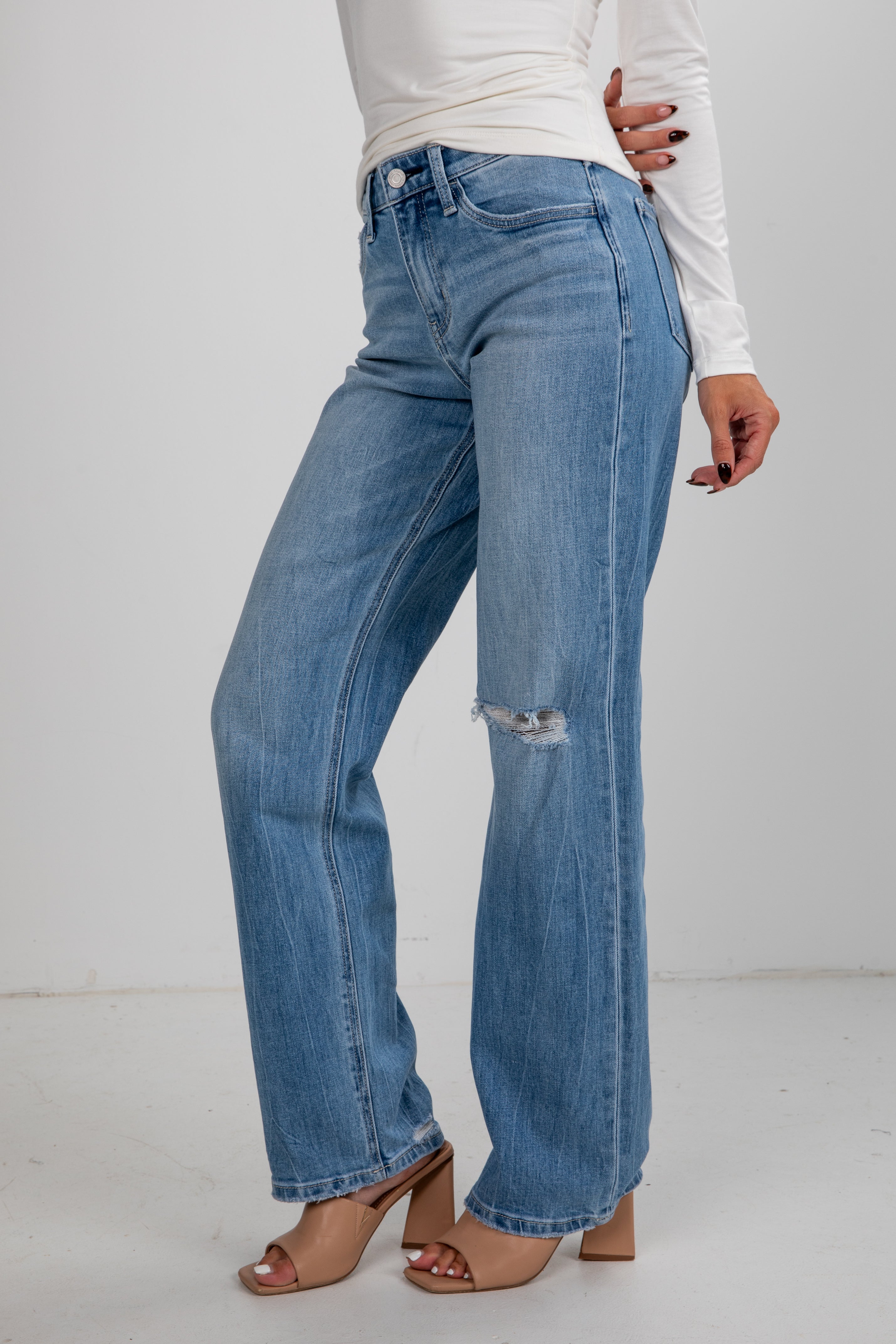 Person wearing blue jeans and a white top on a plain background
