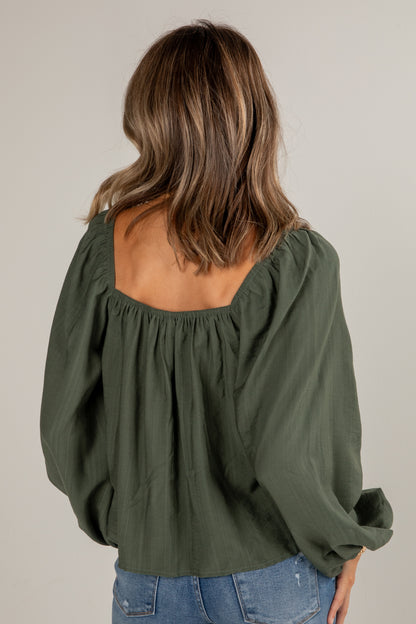 Person wearing an olive green blouse with a plain background