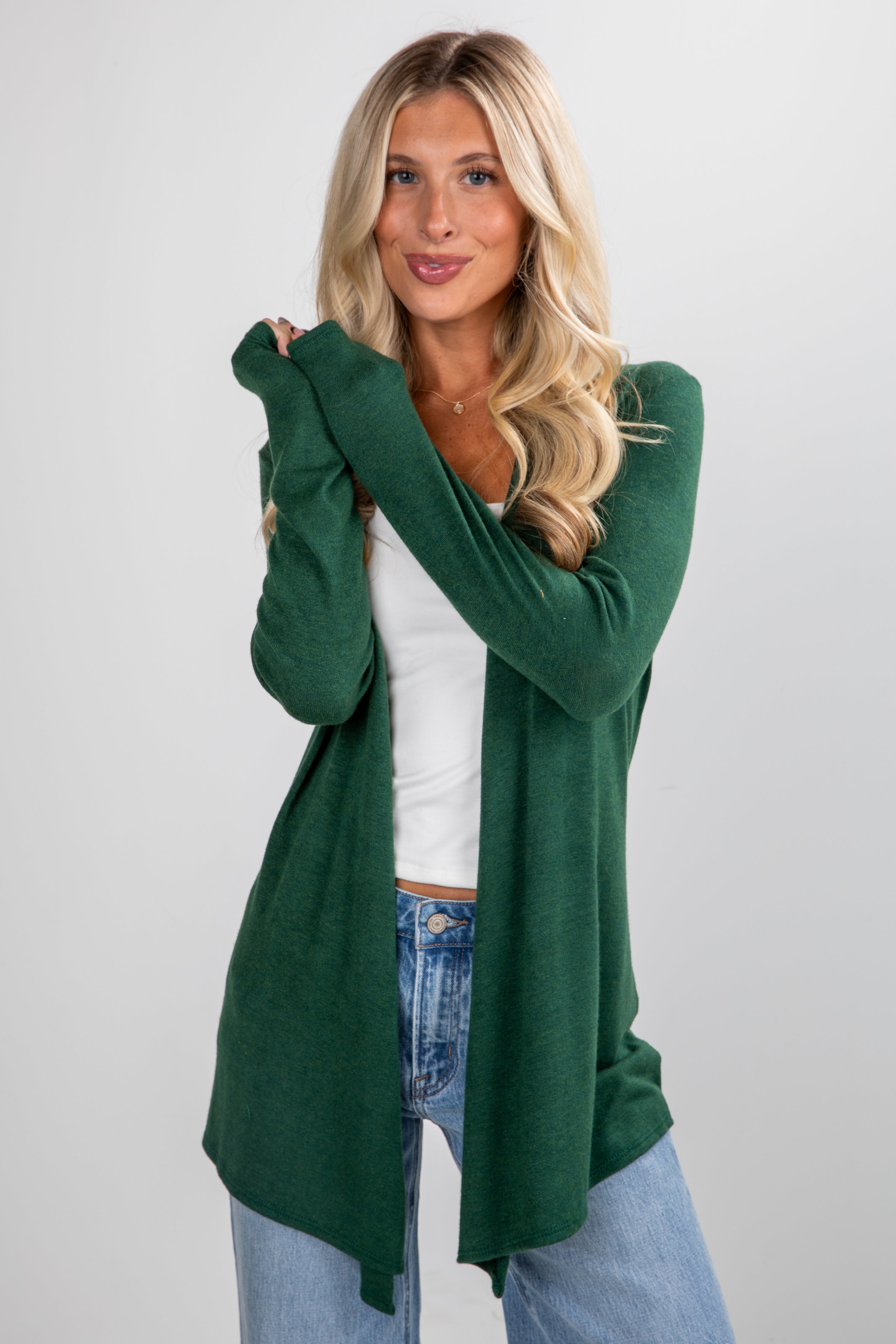 Woman wearing a green cardigan over a white top and blue jeans on a light gray background