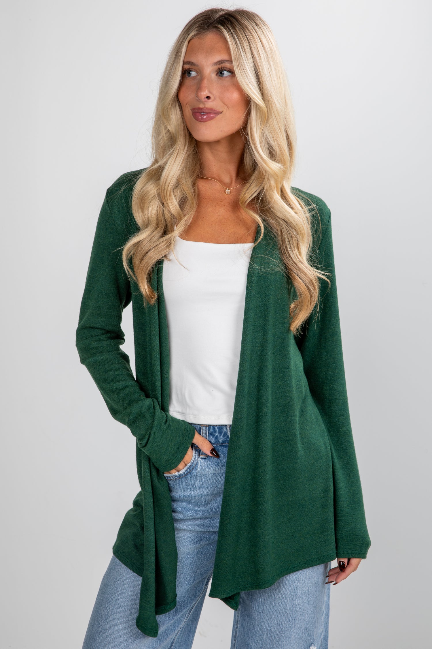 Woman wearing a green cardigan over a white top and blue jeans on a plain background