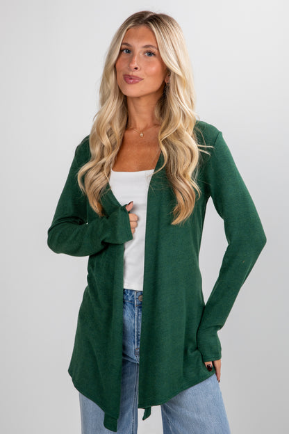 Woman wearing a green cardigan over a white top and blue jeans on a plain background