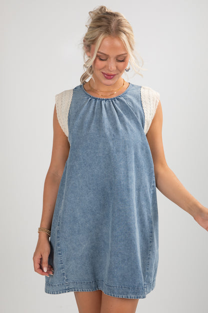 Woman wearing a blue denim dress with white lace sleeves on a plain background