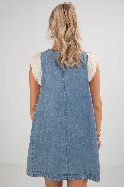 Back view of a person wearing a denim dress with a white lace top on a plain background