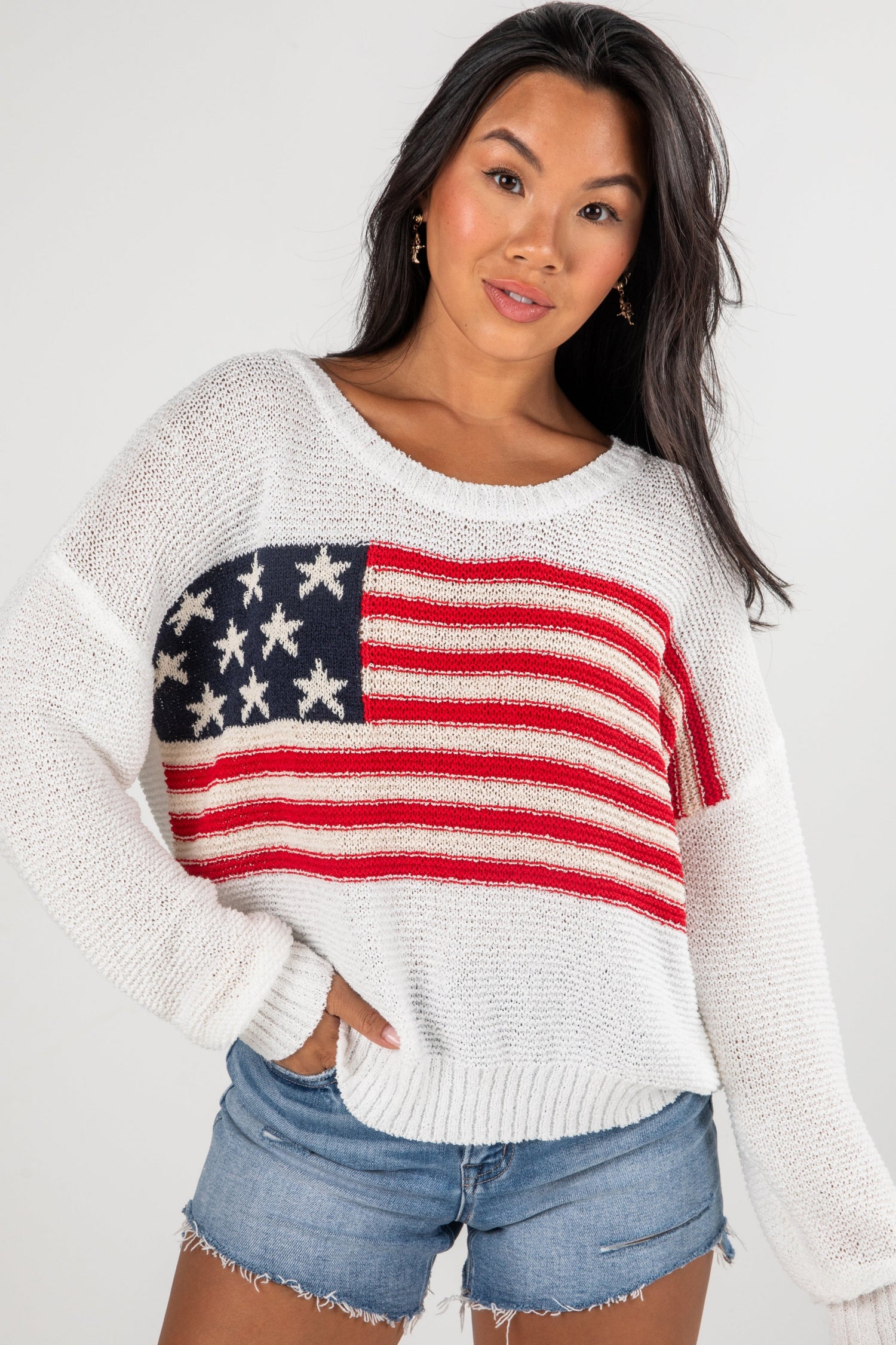 Woman wearing a white sweater with an American flag design on a plain background