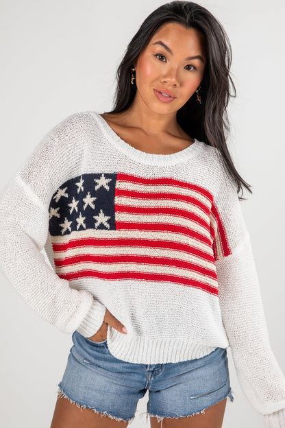 Woman wearing a white sweater with an American flag design on a plain background