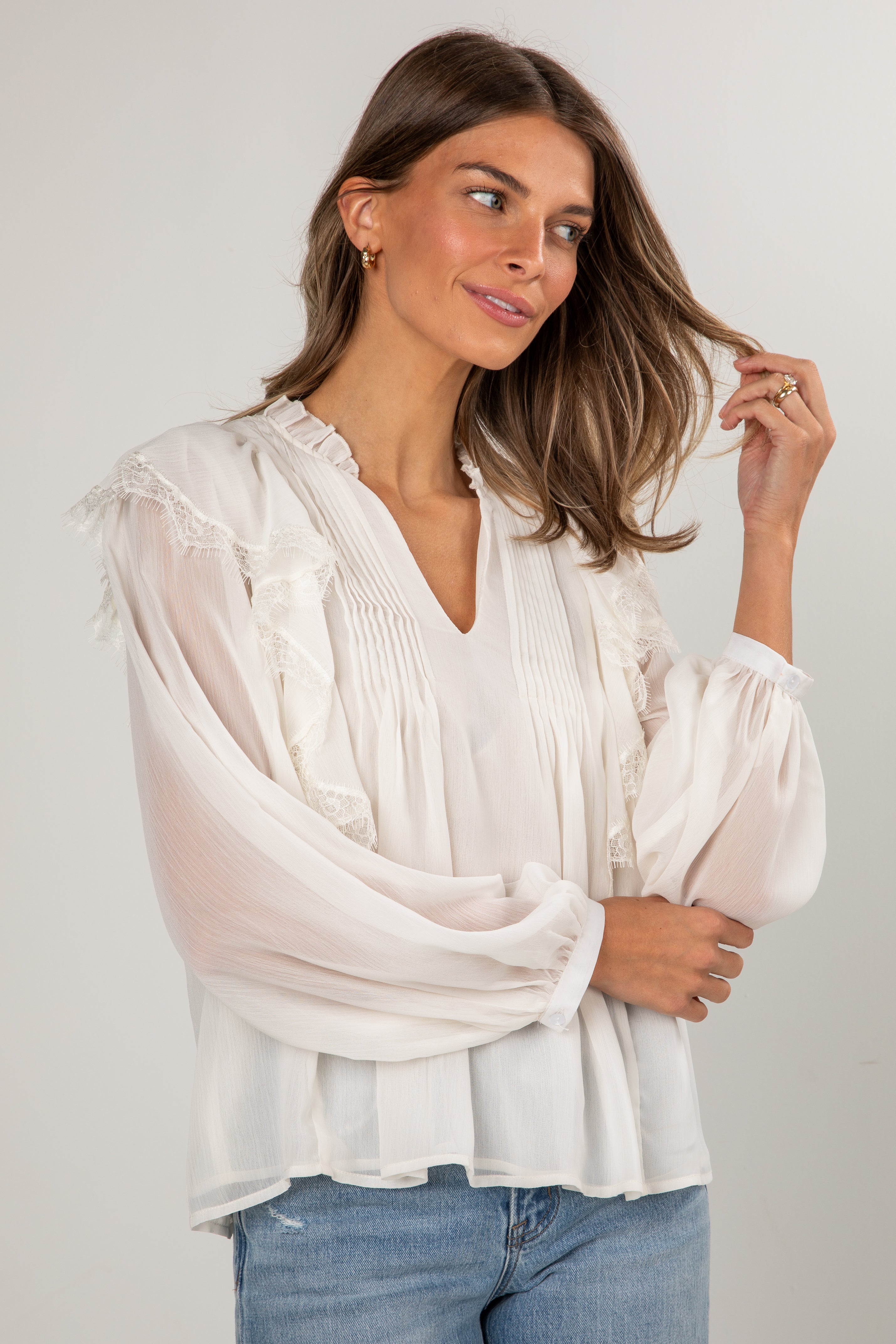 Woman wearing a white blouse with sheer sleeves against a plain background