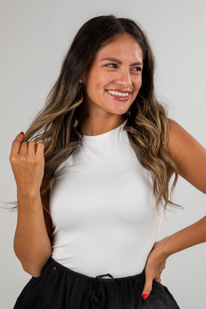 Woman wearing a white sleeveless top and black skirt against a plain background