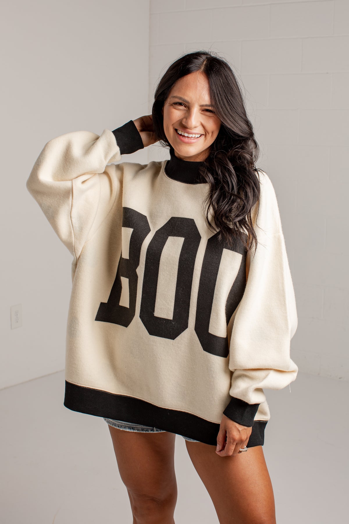 A woman wearing a cream-colored oversized knit sweater with black trim and large black &