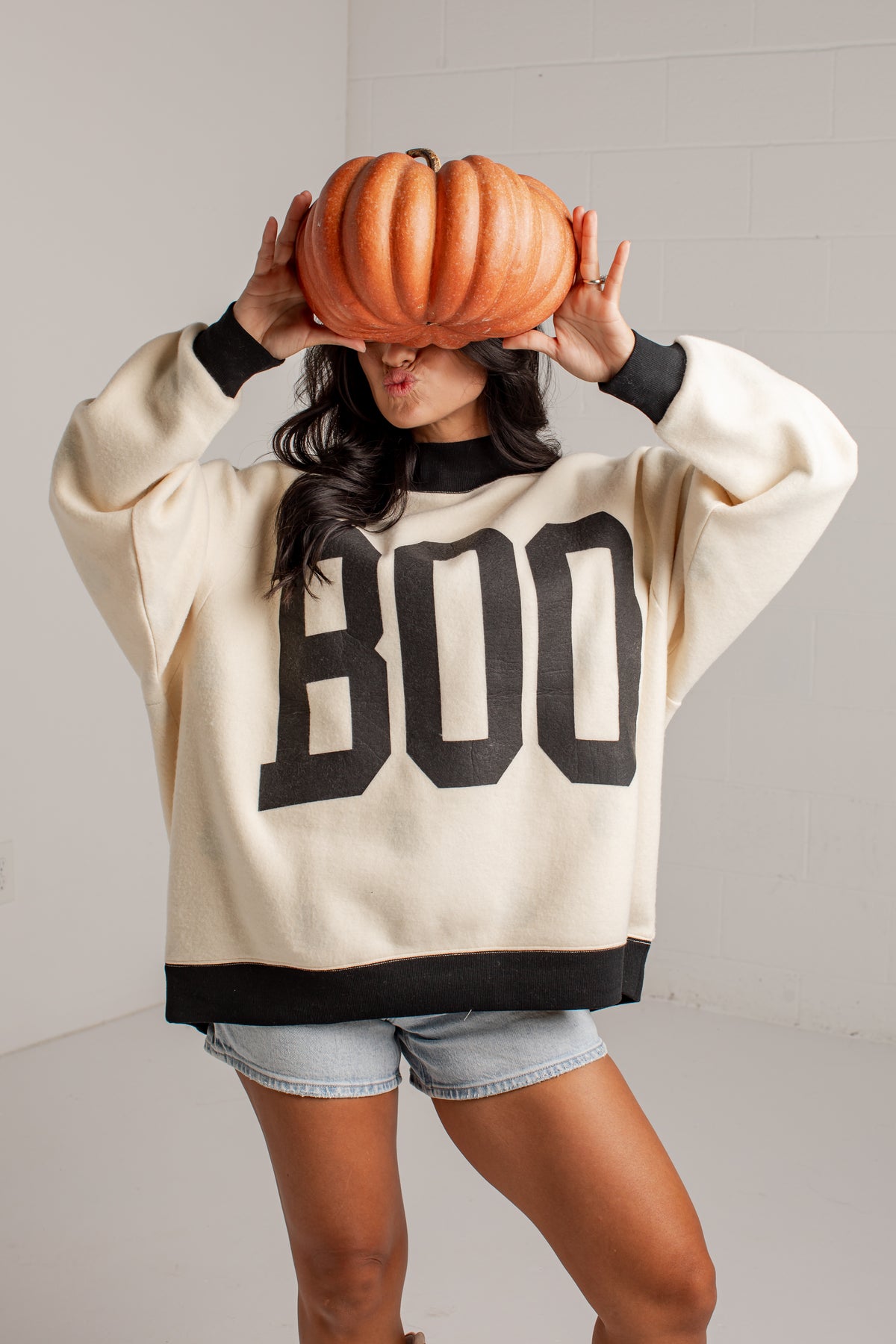 A woman wearing a cream-colored crewneck sweatshirt with &