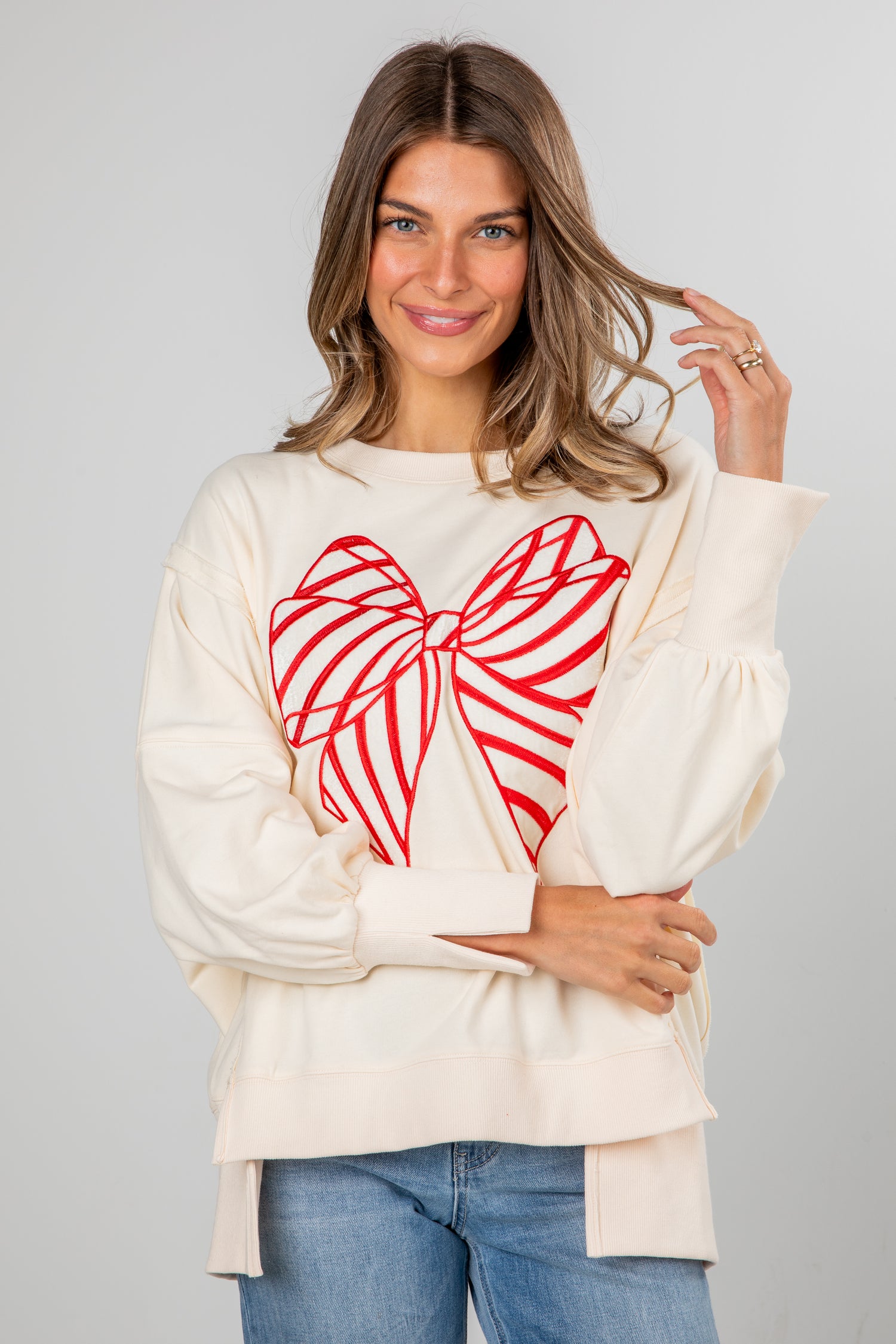 Woman wearing a cream sweater with a red heart design on a gray background