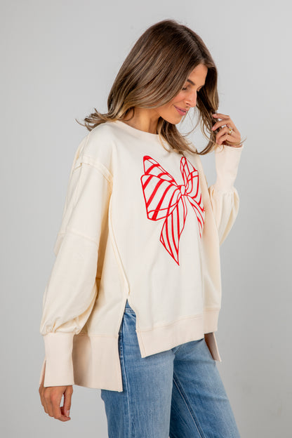 Woman wearing a cream long-sleeve top with a red butterfly design on a gray background
