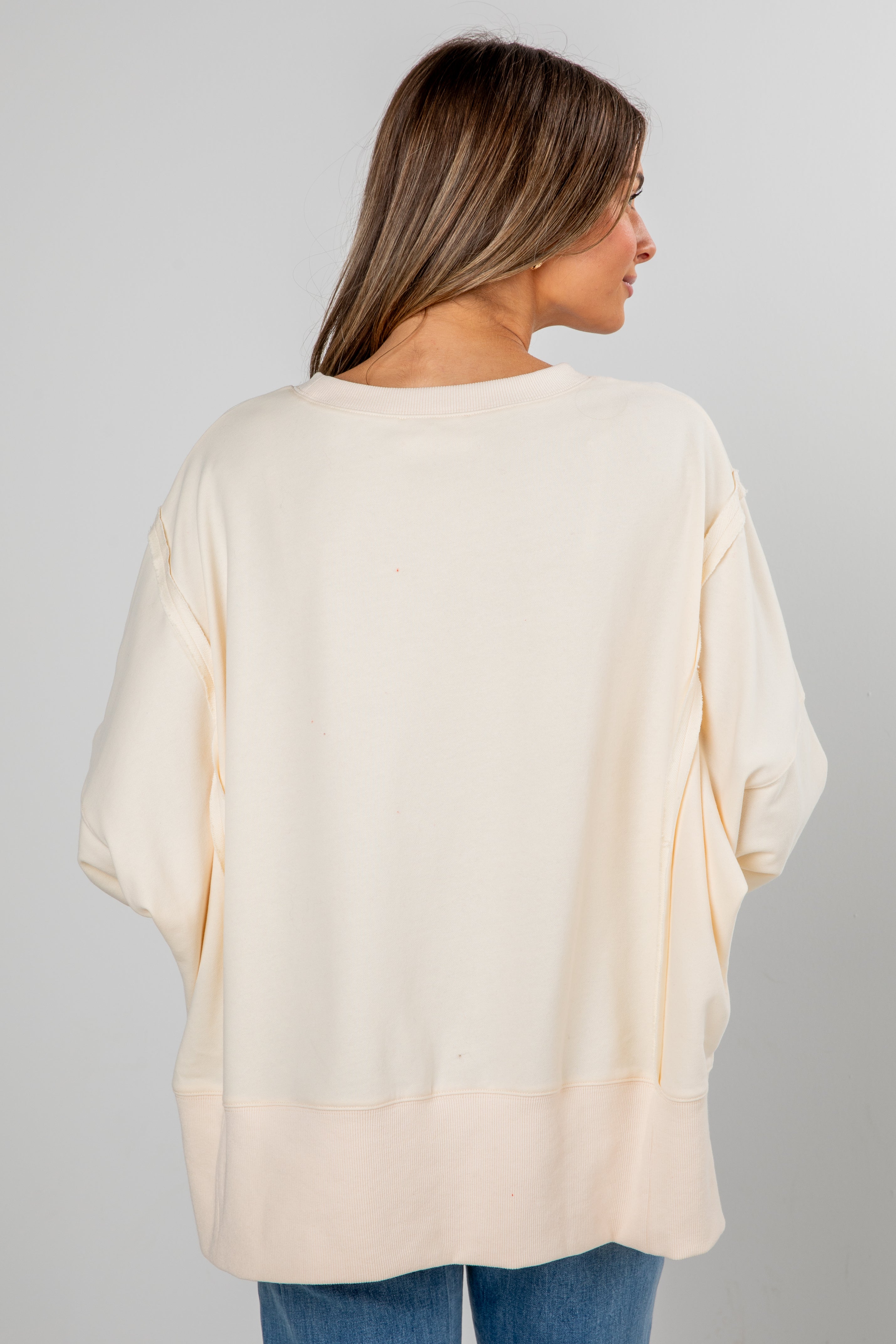 Woman wearing a cream-colored oversized sweater on a plain background
