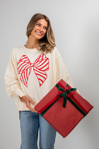 Woman wearing a sweater with a red bow design, holding a large red gift box against a plain background