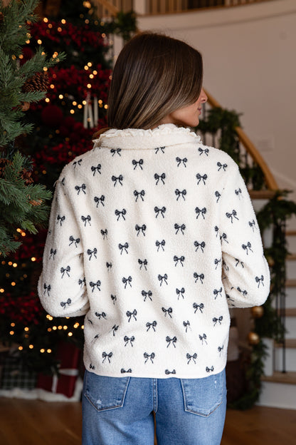 Person wearing a white shirt with black bow pattern in front of a decorated Christmas tree.