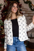 Woman wearing a white blouse with black patterns and blue jeans in a festive indoor setting.
