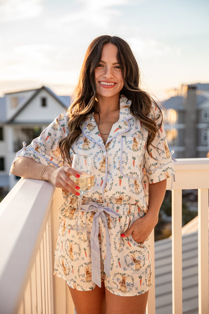 Woman in a floral romper holding a drink on a balcony with a cityscape background