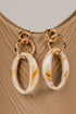 Pair of gold hoop earrings with marbled beige and brown stones on a beige surface.