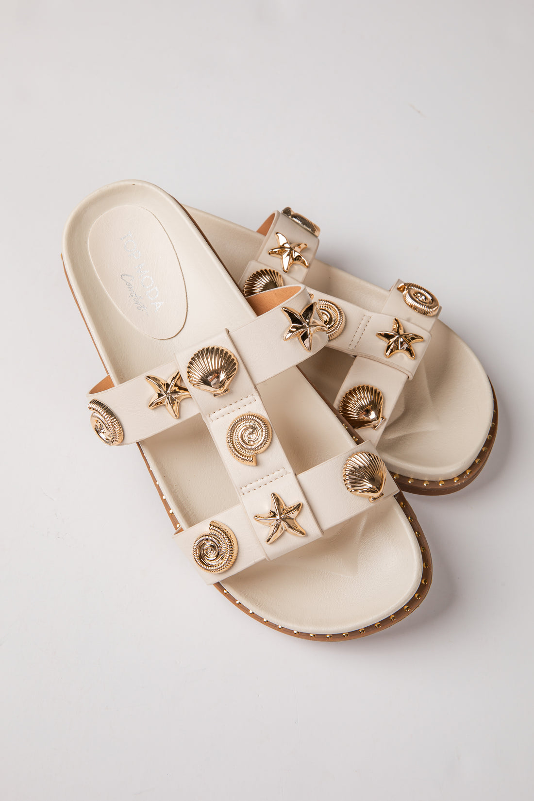 Beige sandals with gold embellishments on a light gray background