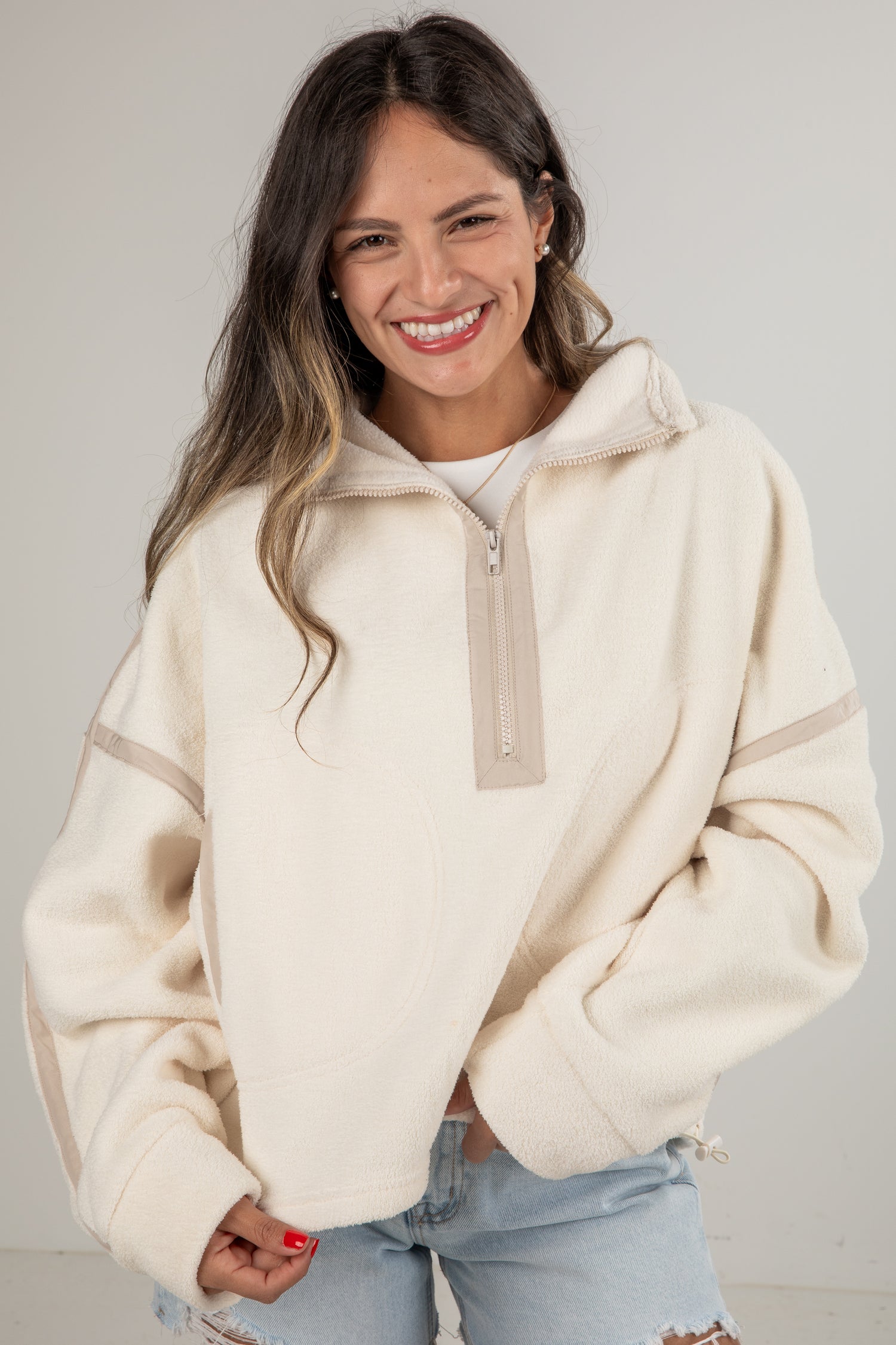Woman wearing a cream-colored fleece pullover with a zipper on a plain background