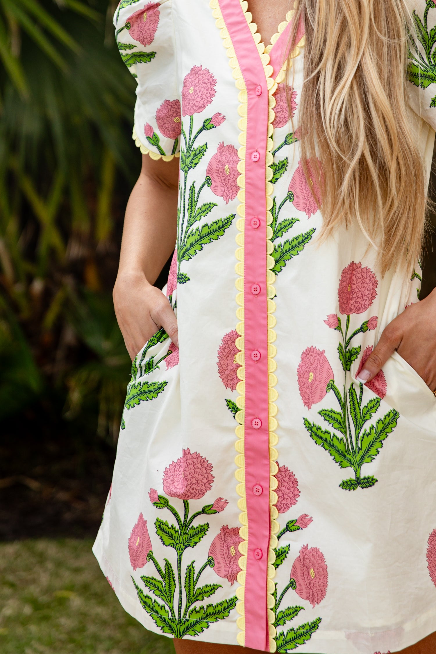 Woman wearing a white dress with pink floral embroidery and a pink border.