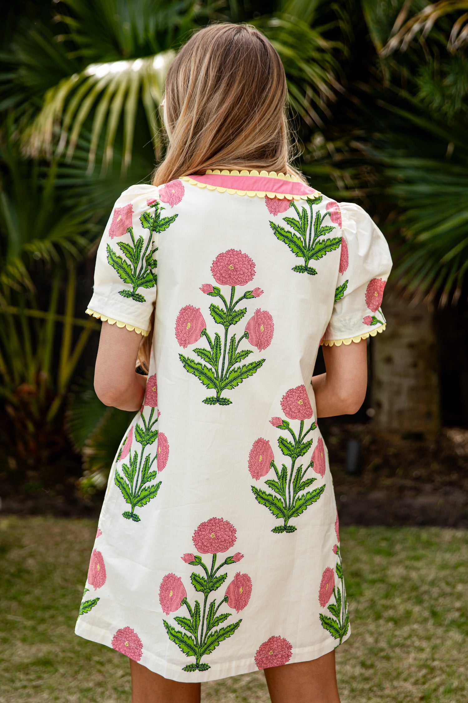 Woman wearing a floral dress with pink flowers and green leaves in an outdoor setting.