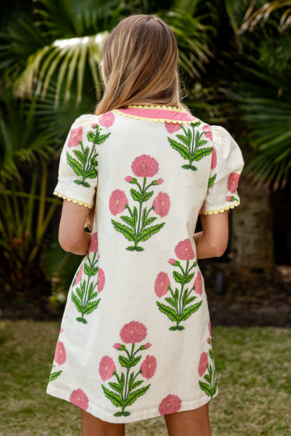 Woman wearing a floral dress with pink flowers and green leaves in an outdoor setting.
