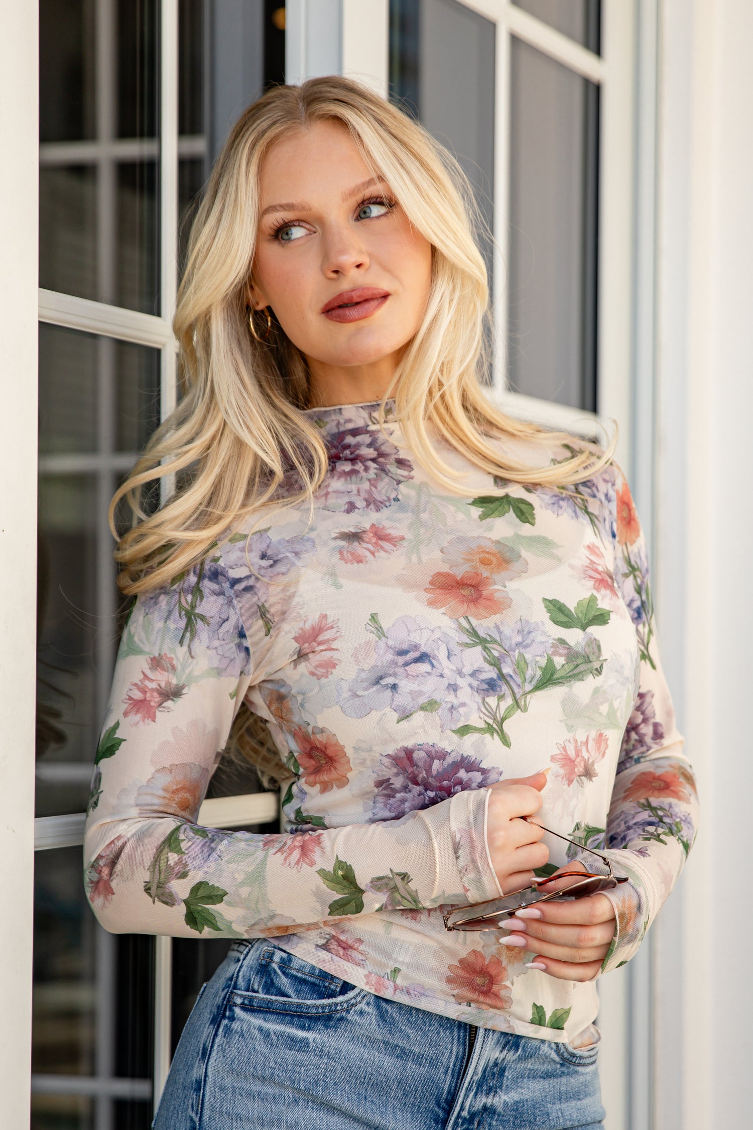 Woman wearing a floral long-sleeve top and jeans standing indoors.