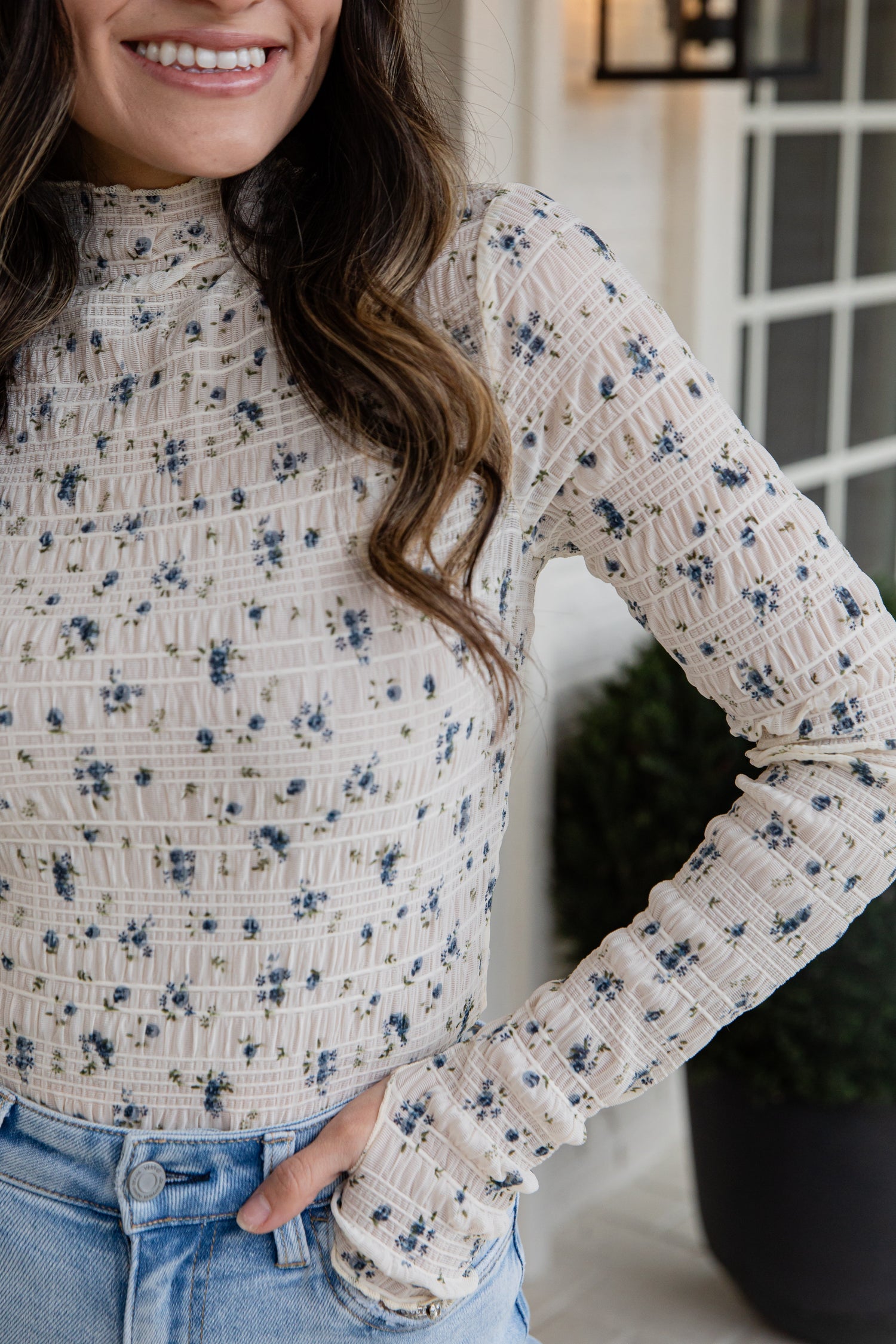 Woman wearing a floral long-sleeve top with a blurred indoor background