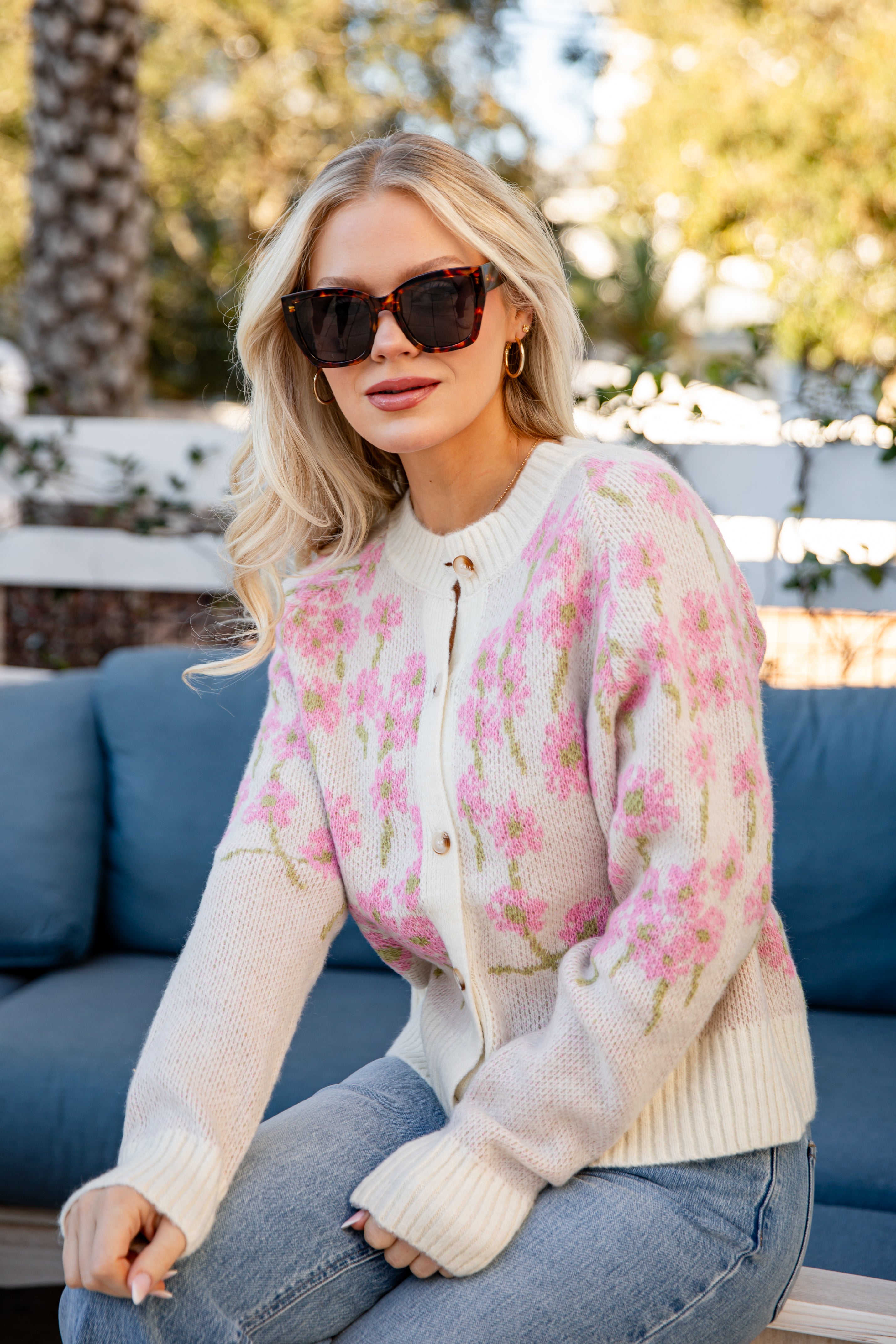 Woman wearing a floral cardigan sitting on a blue couch outdoors.