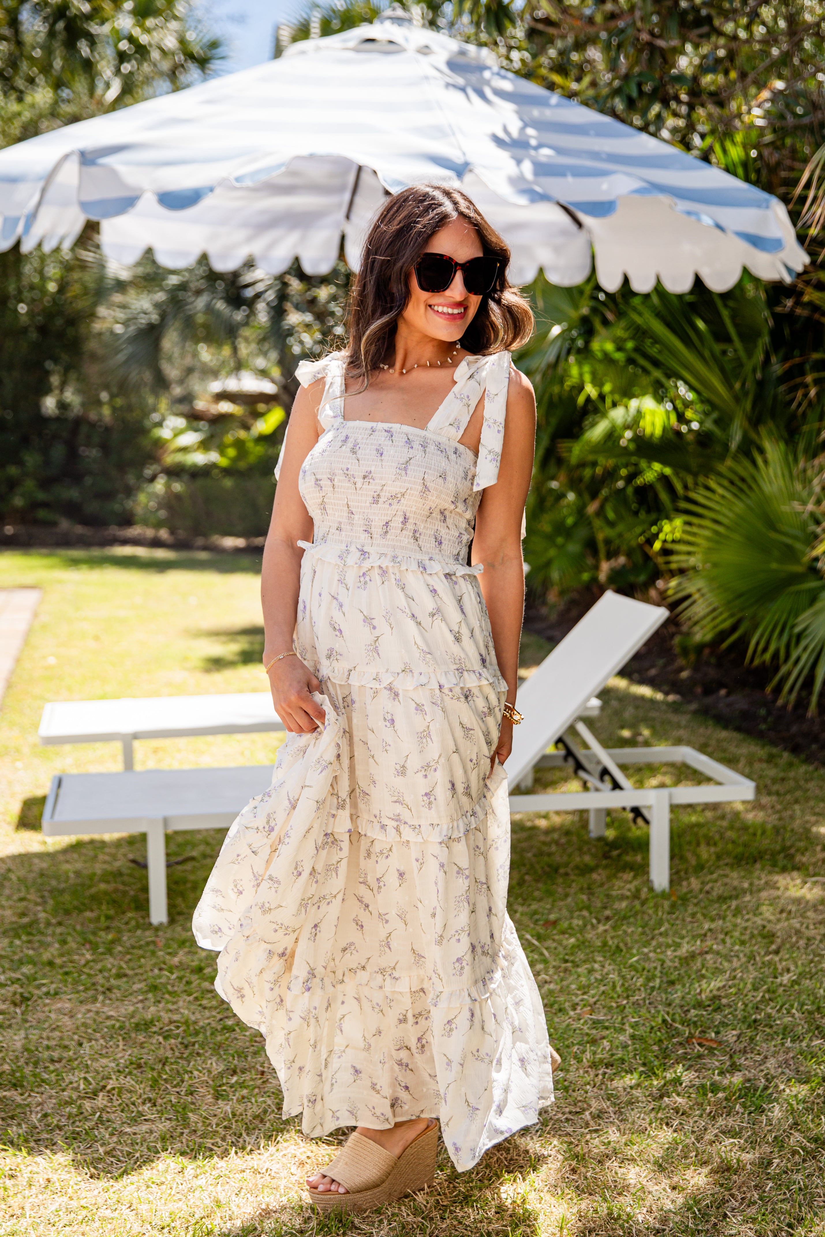 Woman in a floral dress standing under a striped umbrella in a garden setting