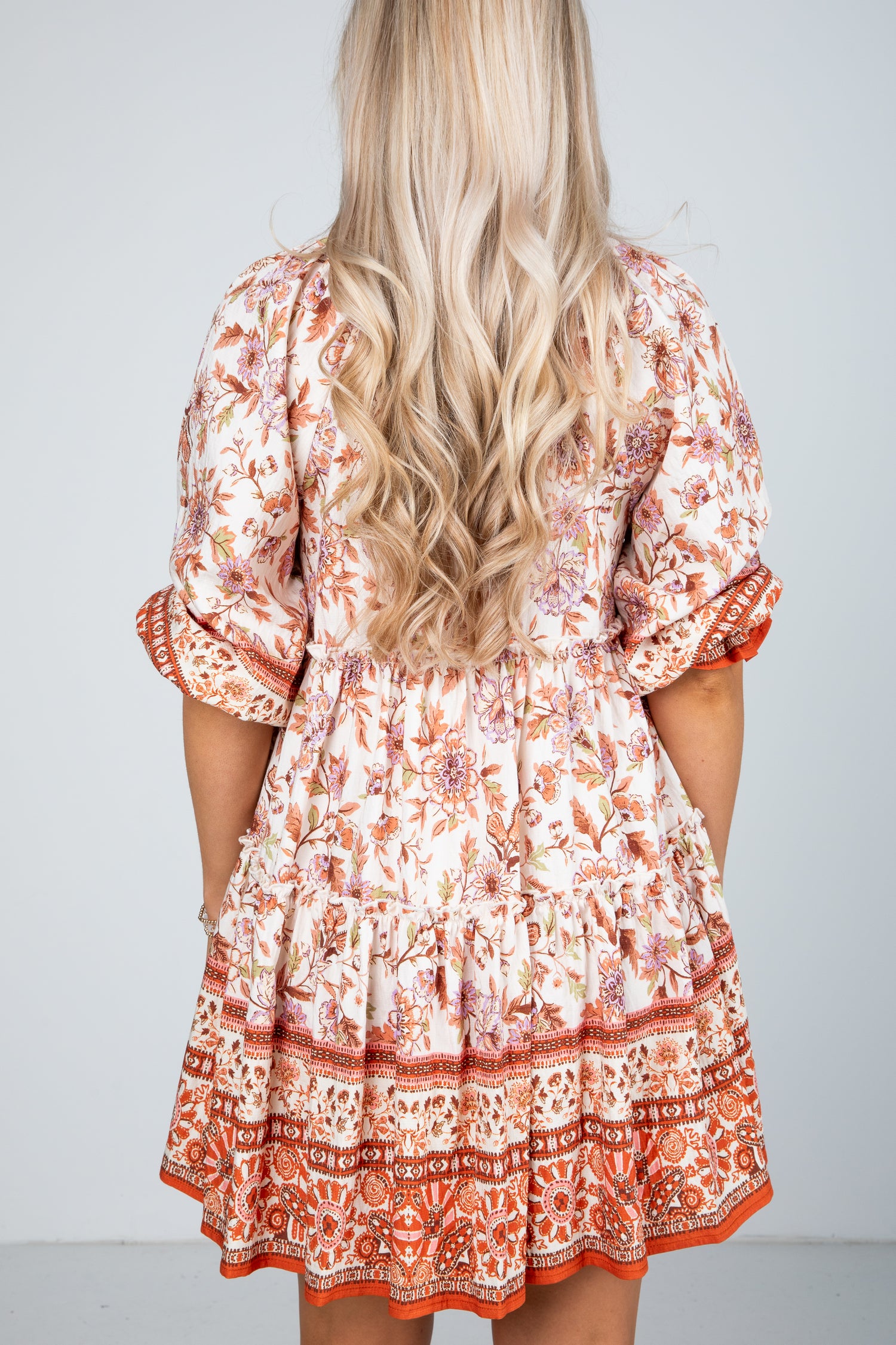 Woman wearing a patterned dress with long blonde hair on a plain background