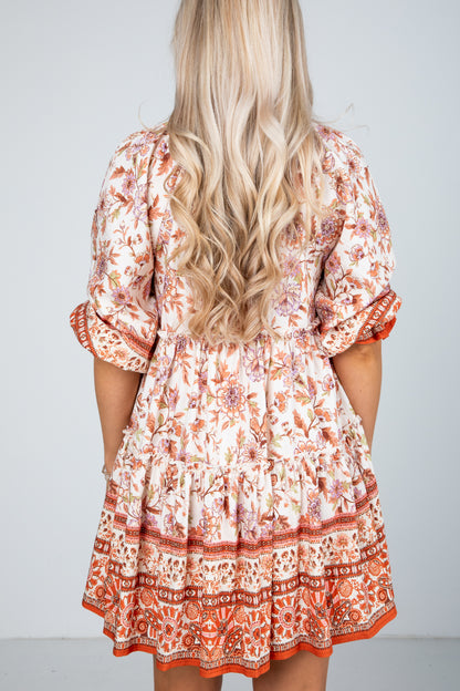 Woman wearing a patterned dress with long blonde hair on a plain background