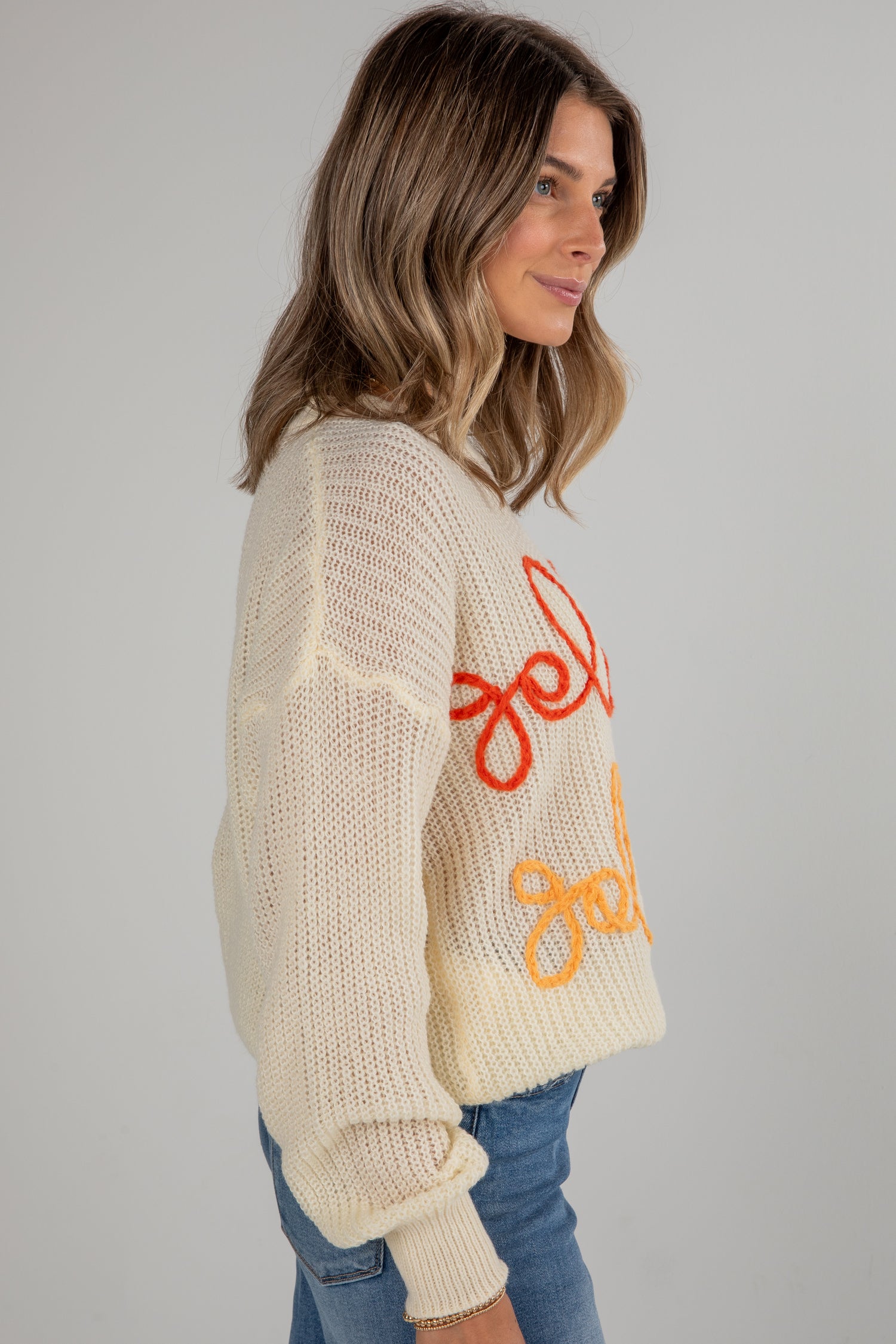 Woman wearing a cream sweater with colorful text on a plain background