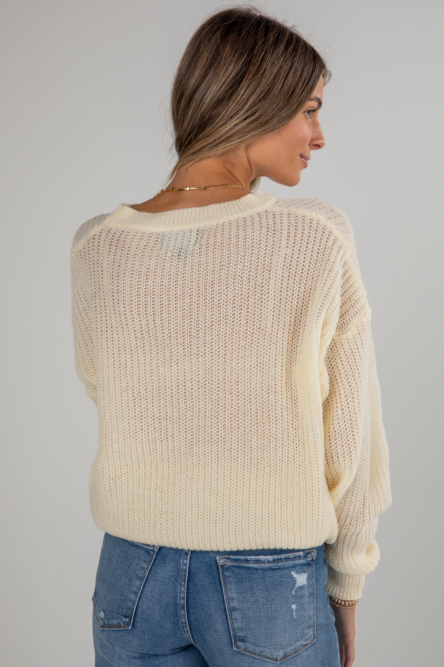 Woman wearing a beige knitted sweater and blue jeans on a gray background