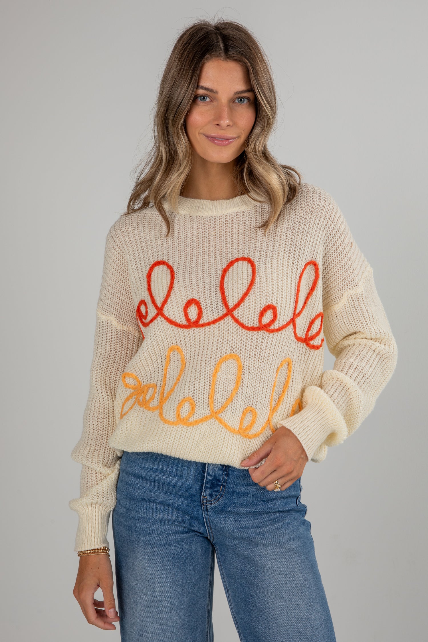 Woman wearing a cream sweater with colorful text design on a plain background
