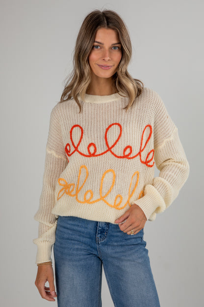 Woman wearing a cream sweater with colorful text design on a plain background