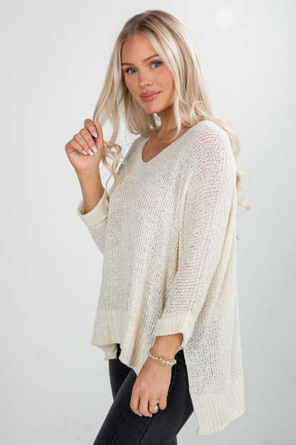 Woman wearing a beige knit poncho against a white background