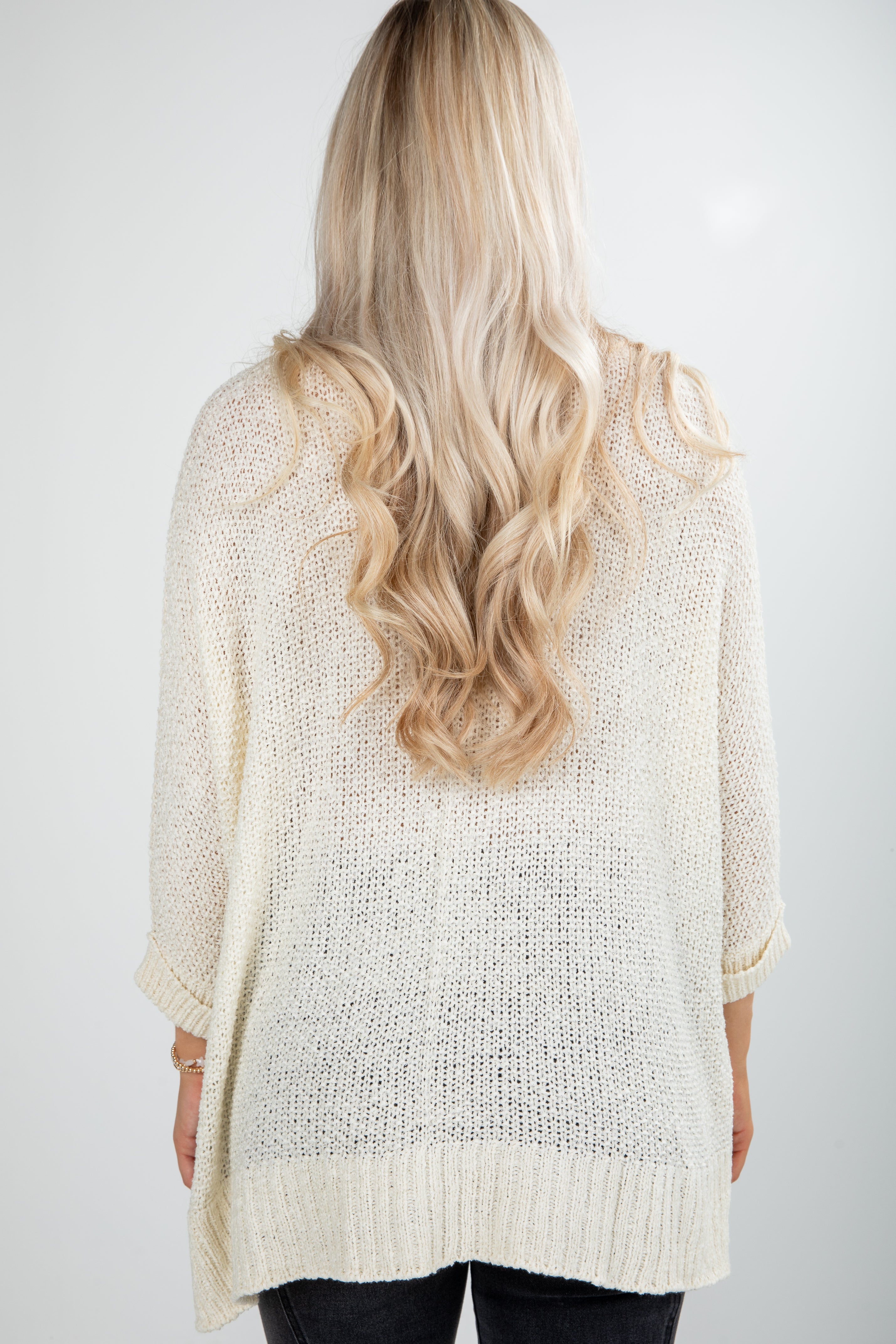 Back view of a person wearing a light beige knitted cardigan on a white background