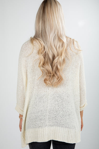 Back view of a person wearing a light beige knitted cardigan on a white background