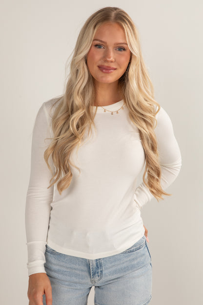 Woman wearing a white long-sleeve top and light blue jeans against a plain background