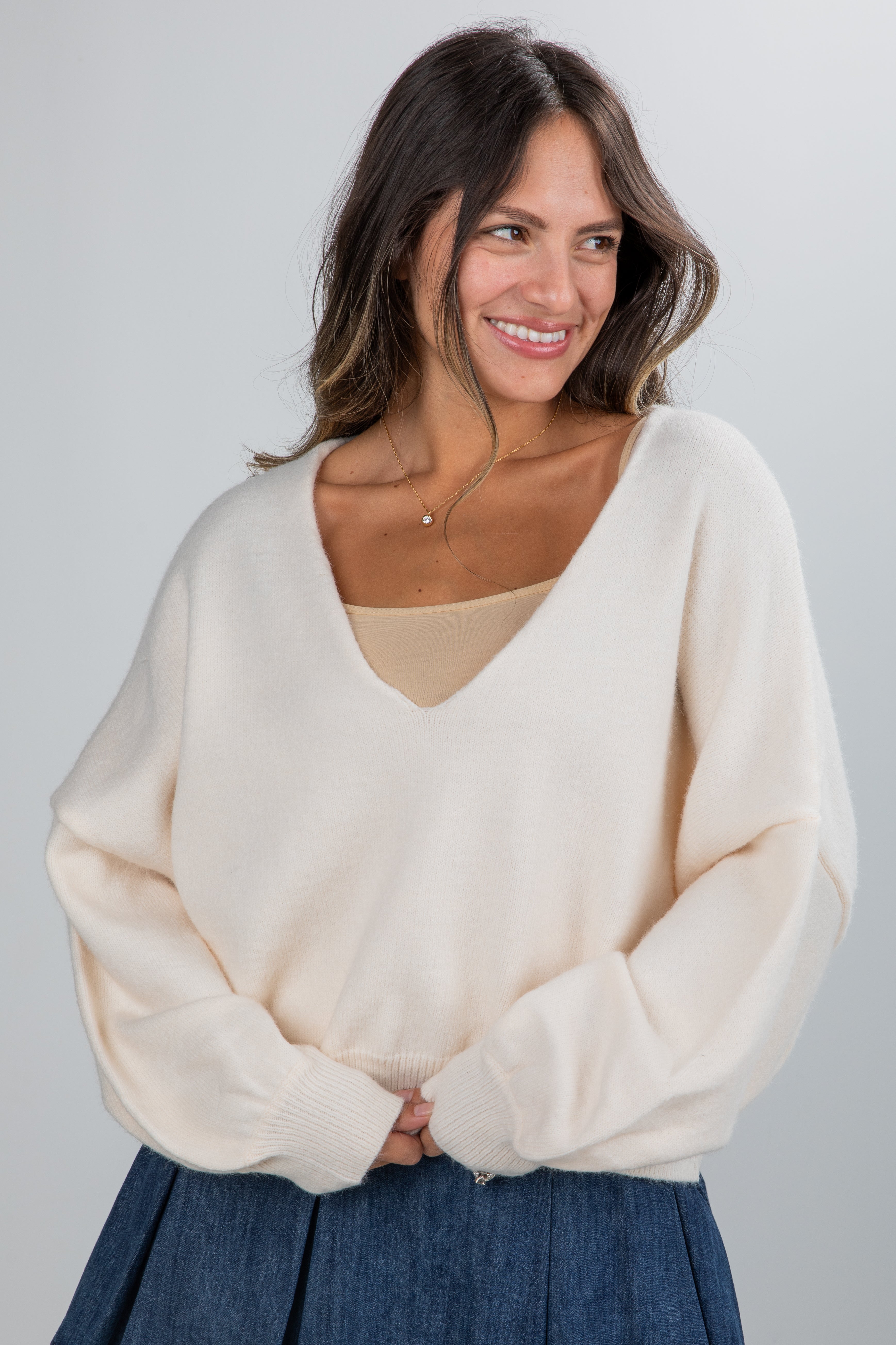 Woman wearing a cream sweater over a beige top with a plain background