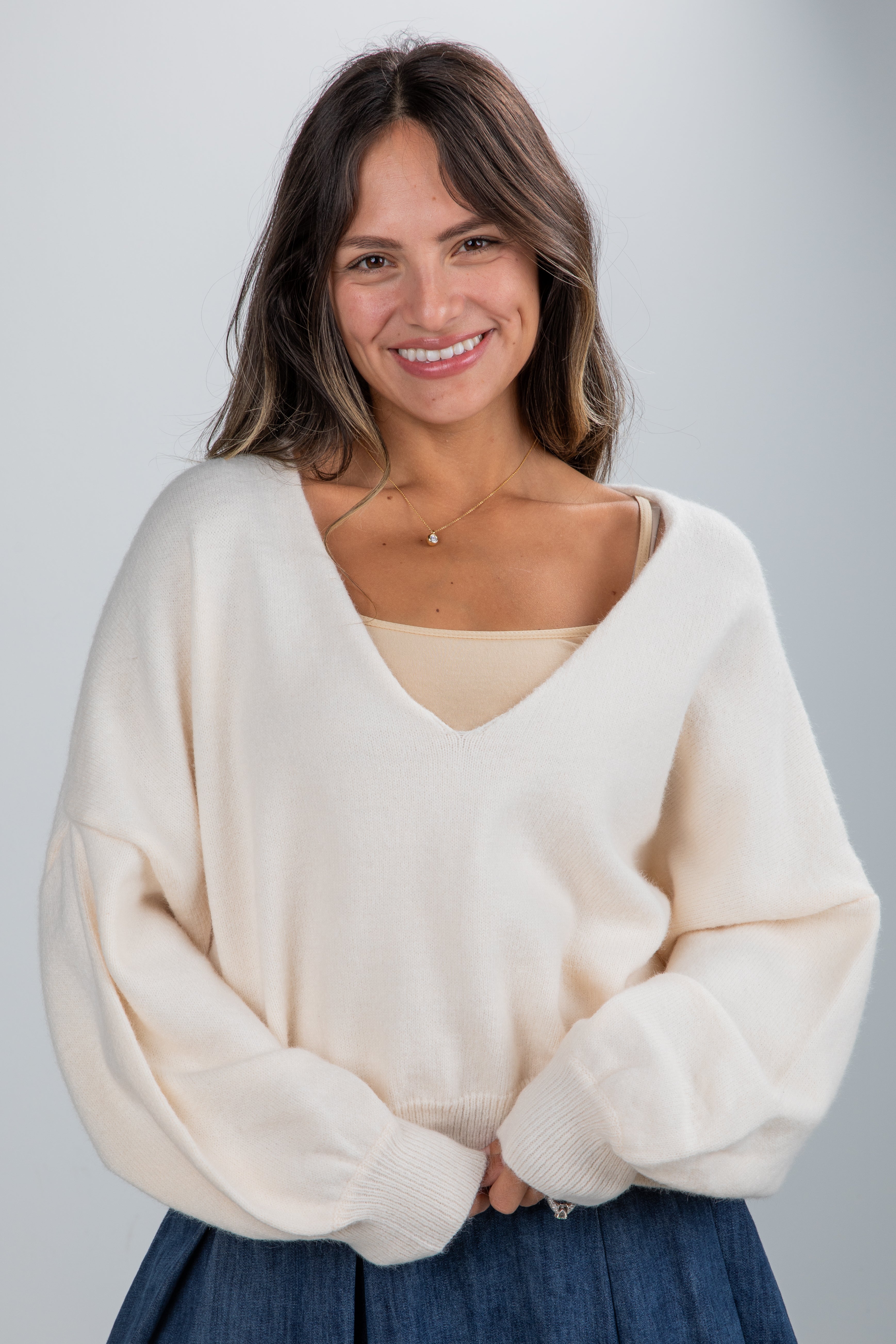 Woman wearing a cream sweater and blue skirt against a plain background