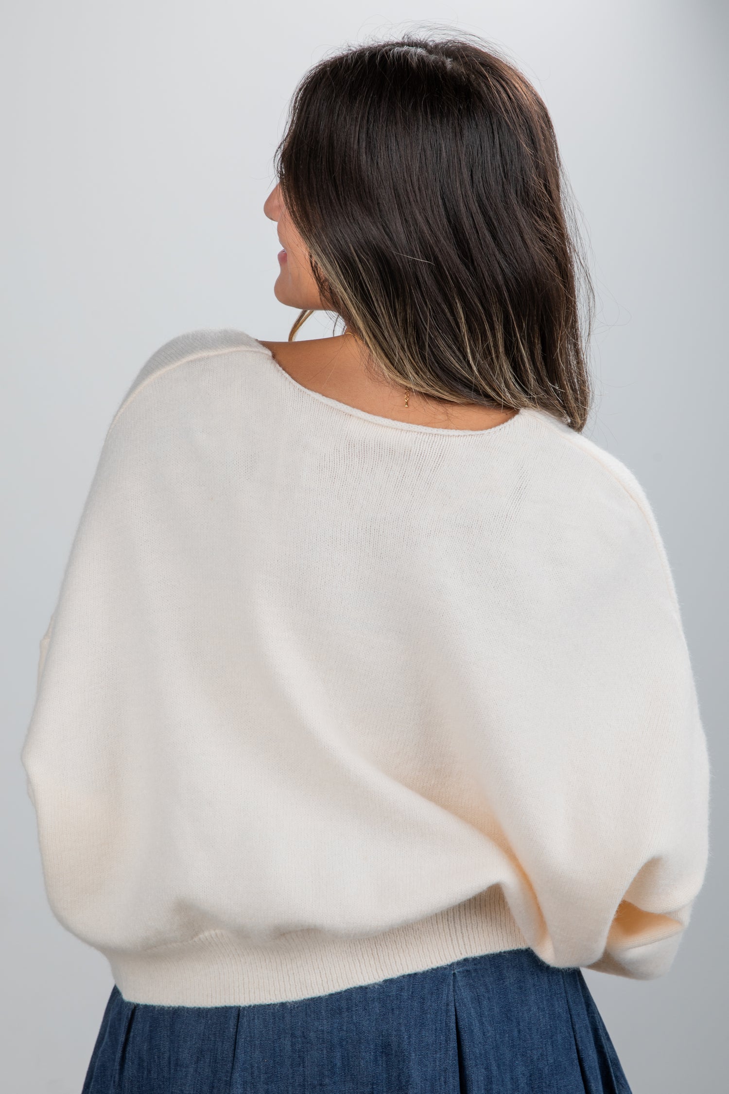 Woman wearing a cream sweater and blue skirt on a plain background