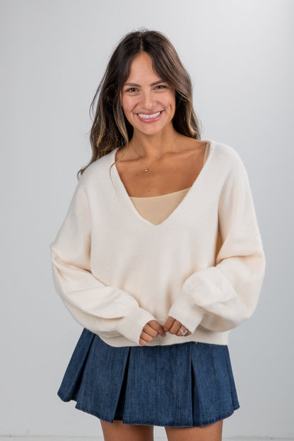 Woman wearing a cream sweater and blue skirt against a white background