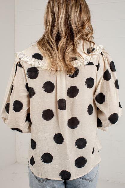 A woman viewed from behind wearing a cream-colored blouse with large black polka dots and a lace collar, paired with light blue jeans.