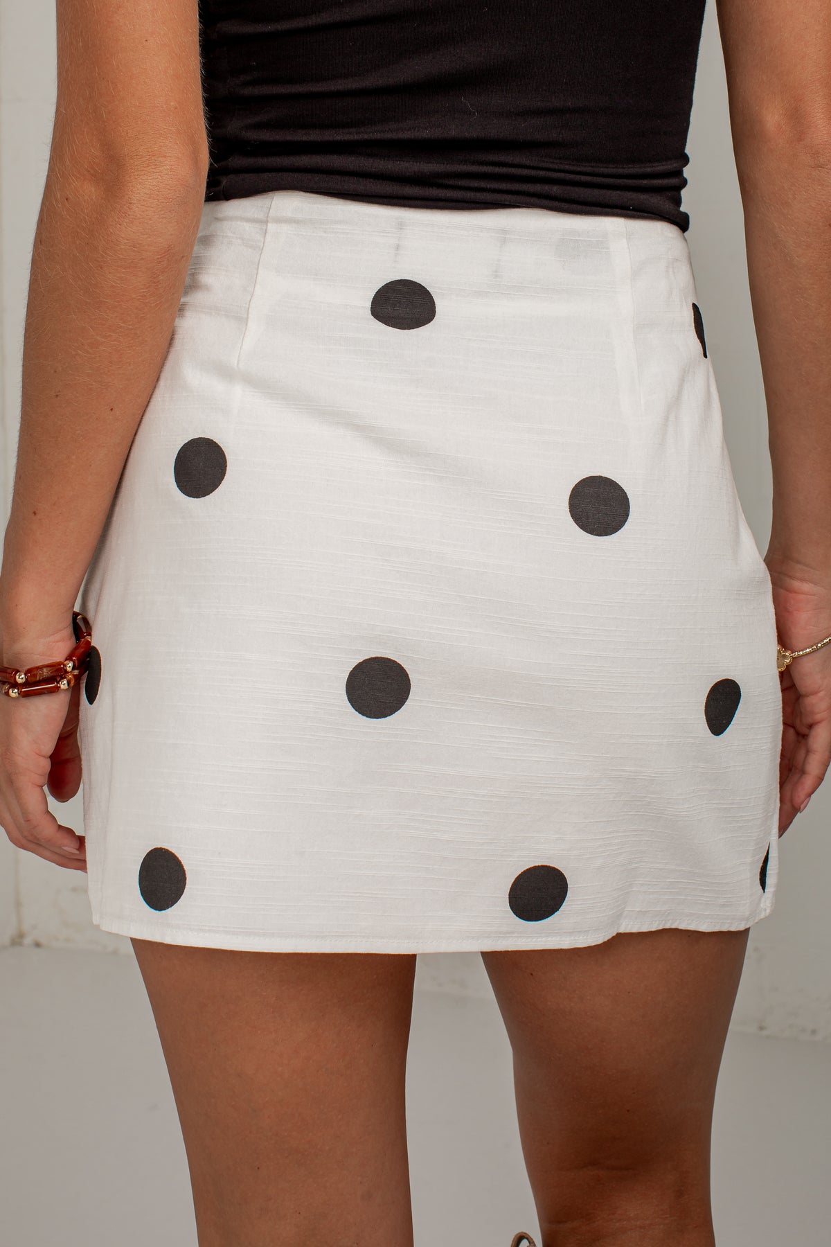 A white mini skirt with black polka dots, worn by a model with a black top, shown from the back.