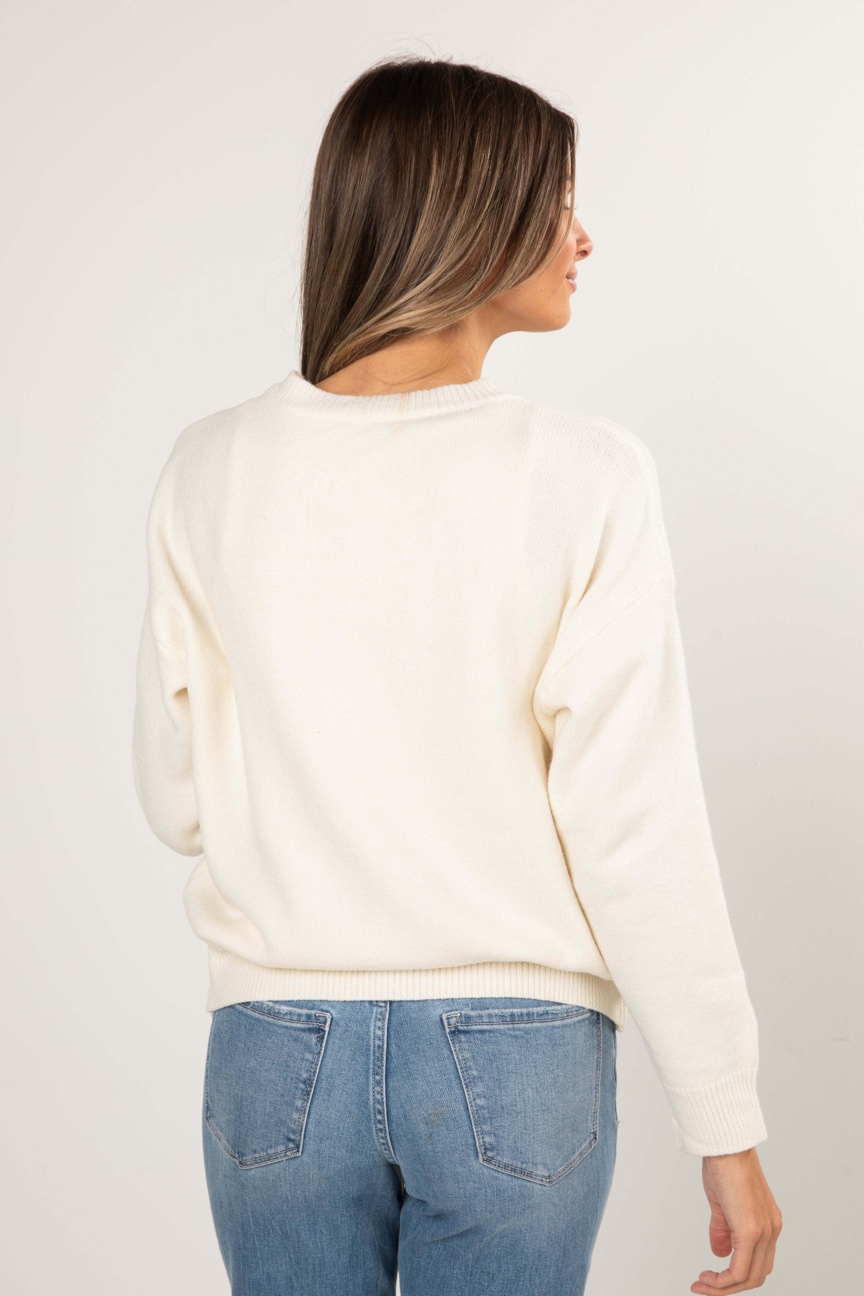 Woman wearing a cream sweater and blue jeans on a white background