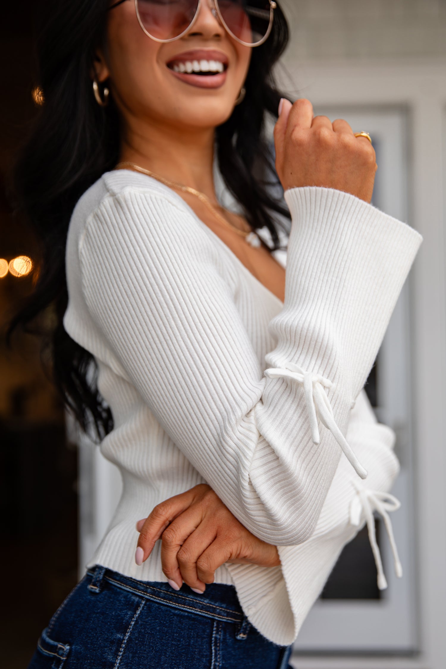 Woman wearing a white ribbed sweater with ruffled sleeves and blue jeans.